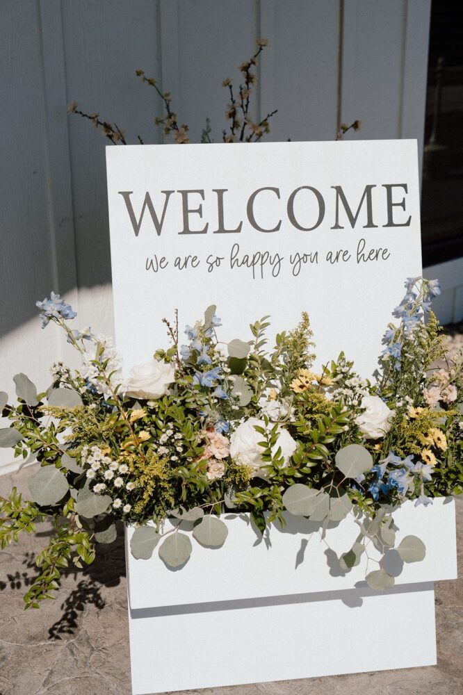 Welcome sign decorated with blue, white, peach, and yellow wedding wildflowers