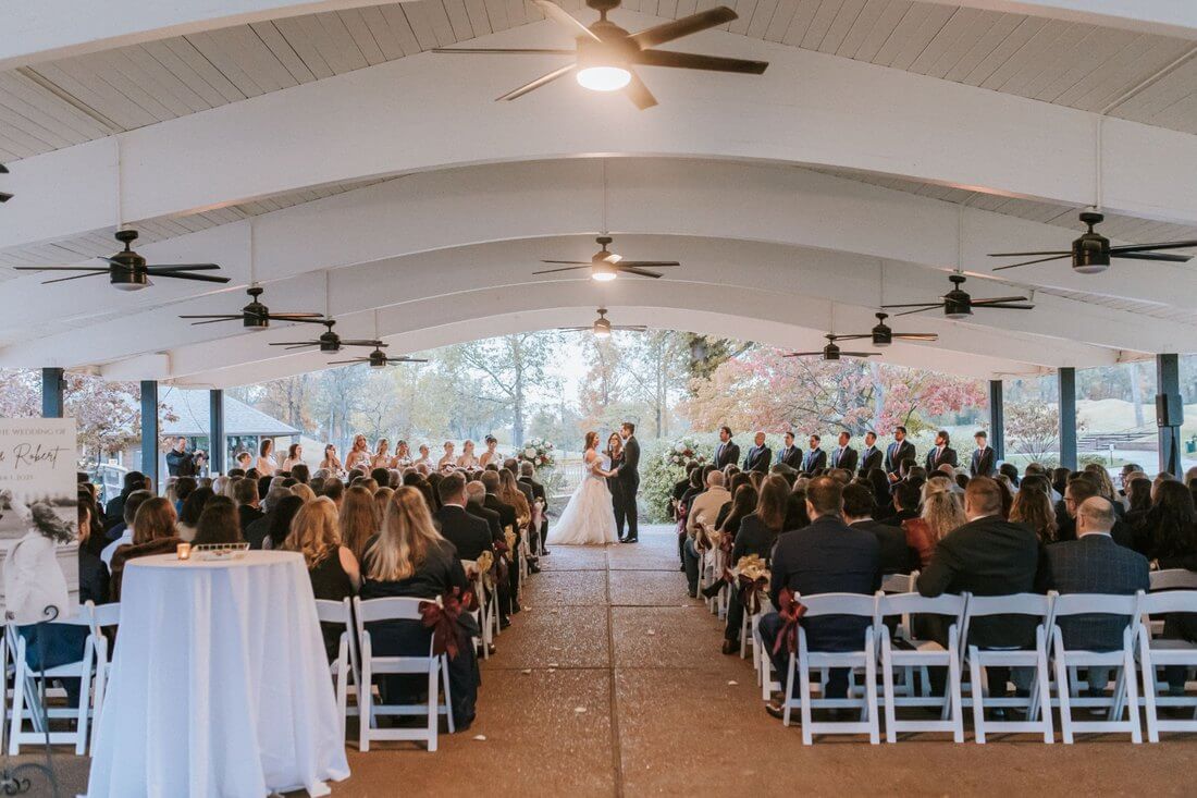 Wedding ceremony in the lower pavilion at Whitmoor Country Club with large floral arrangements flanking the couple