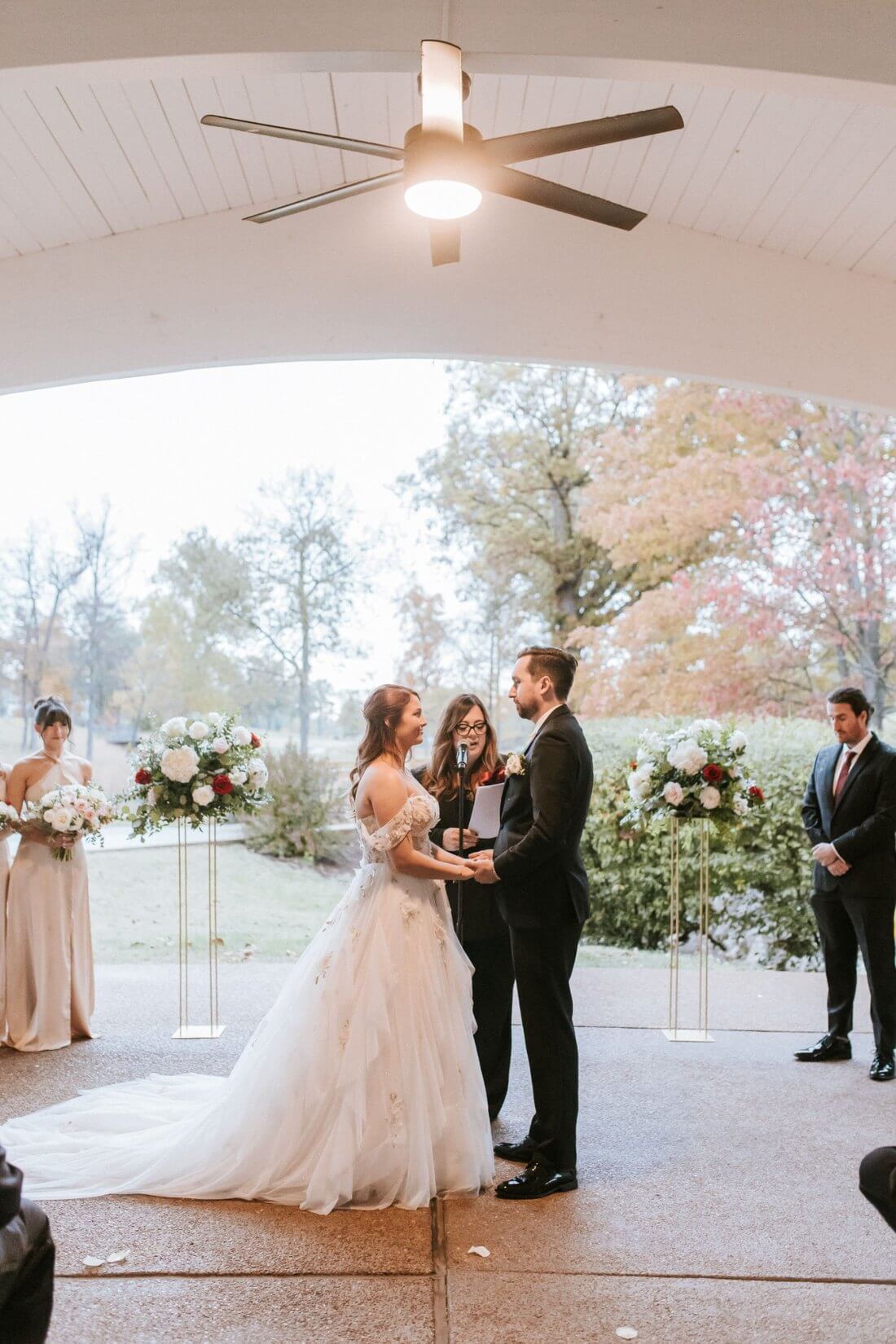 Bride and groom exchanging vows between large blush and white floral arrangements at Whitmoor Country Club