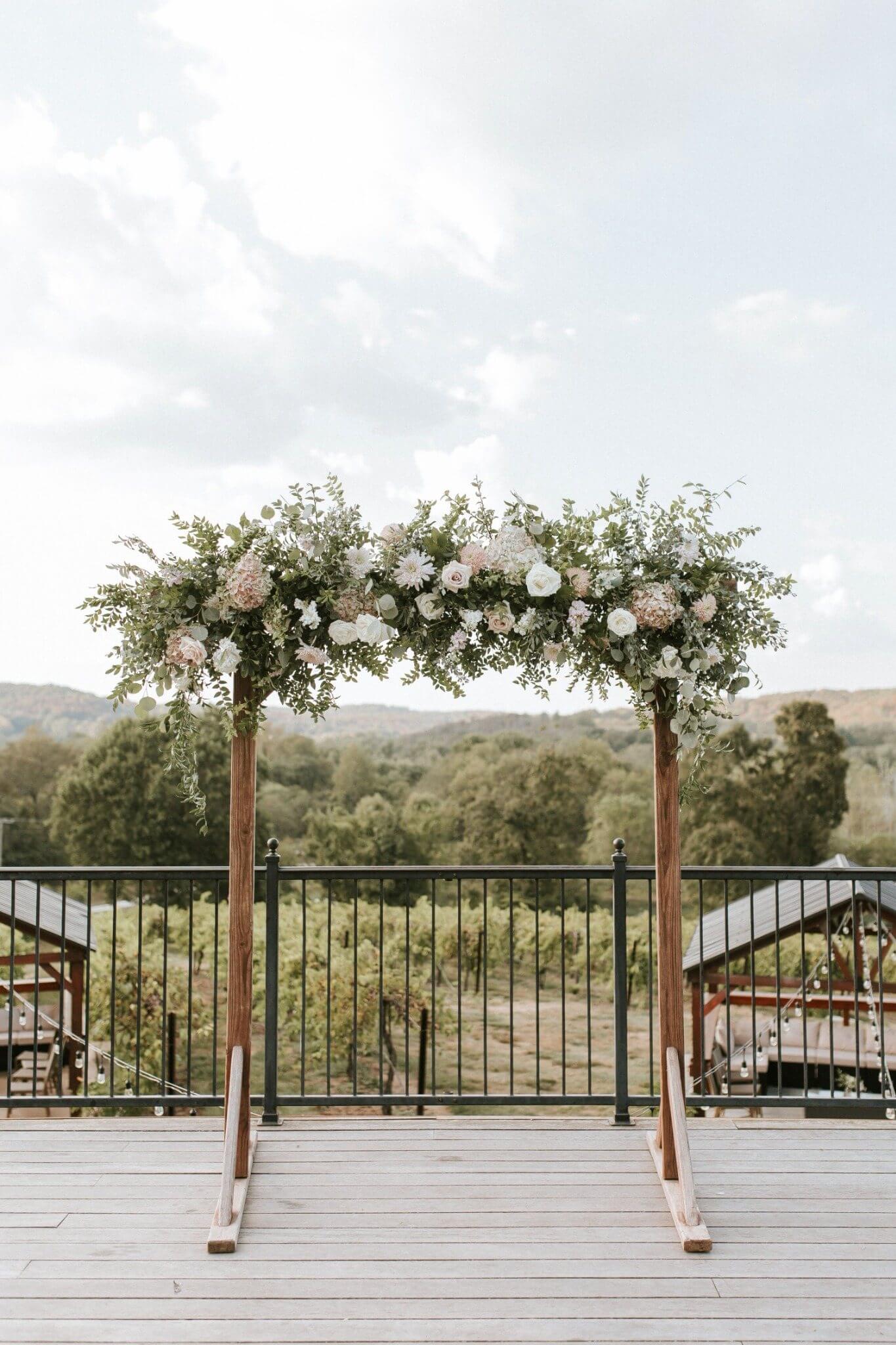 Wooden wedding arbor covered with neutral fall flowers, burgundy accents, and greenery at Chandler Hill