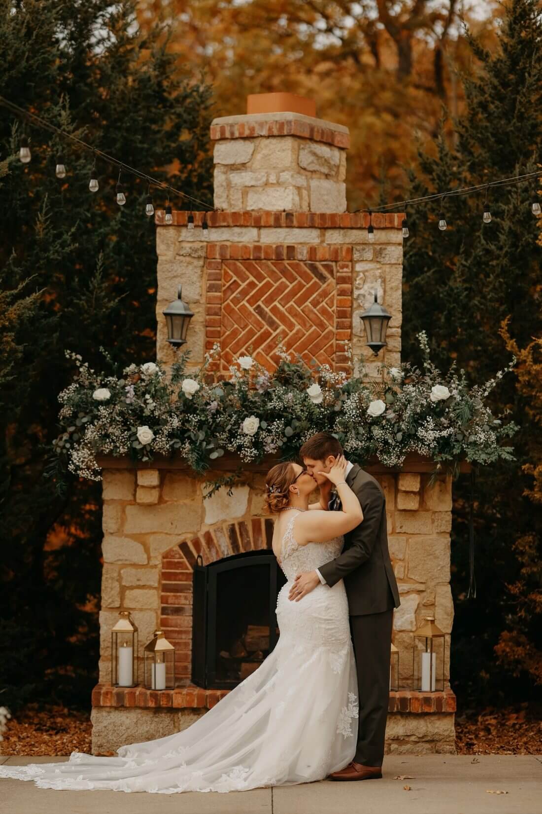 Bride and groom kissing in front of a flower-covered stone fireplace at Silver Oaks Chateau