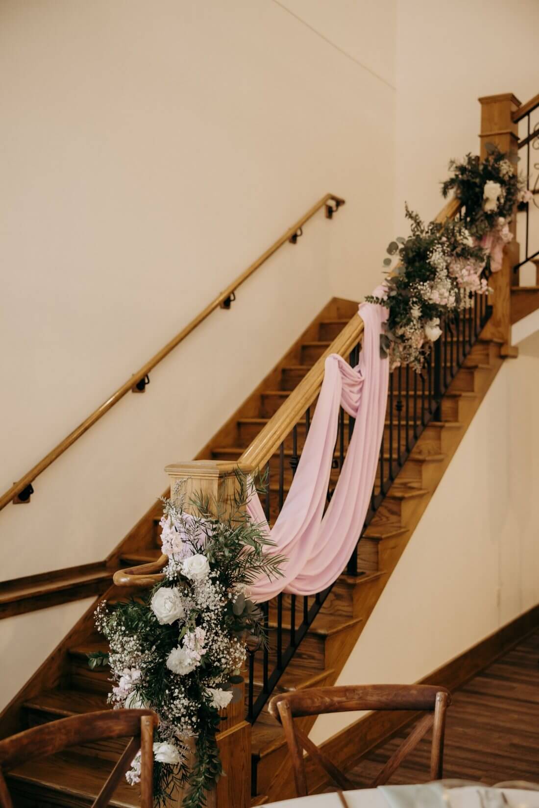 White flowers, greenery, and pink fabric draped along the wooden staircase at Silver Oaks Chateau