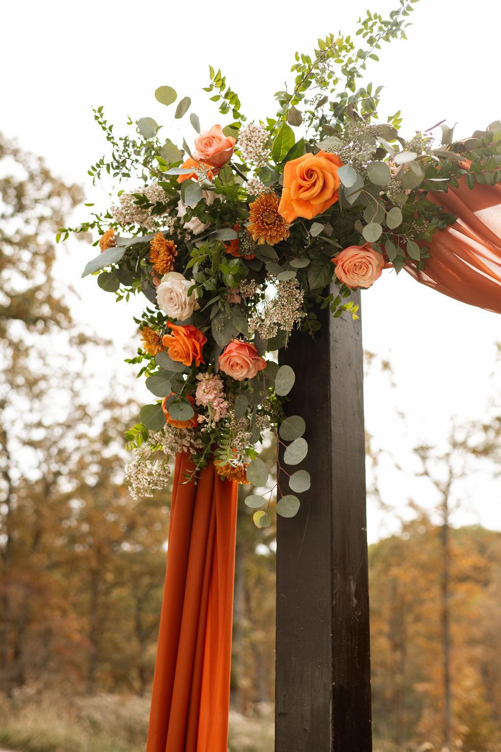 Orange roses, mums, waxflower and greenery decorating an autumn wedding arbor at Silver Oaks Chateau