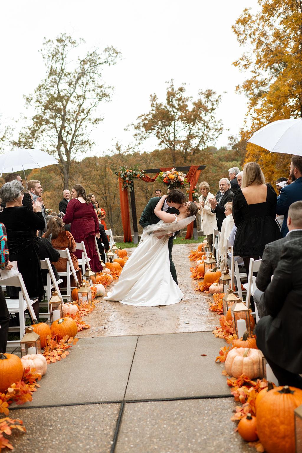 Newlyweds celebrating on an autumn wedding aisle lined with pumpkins