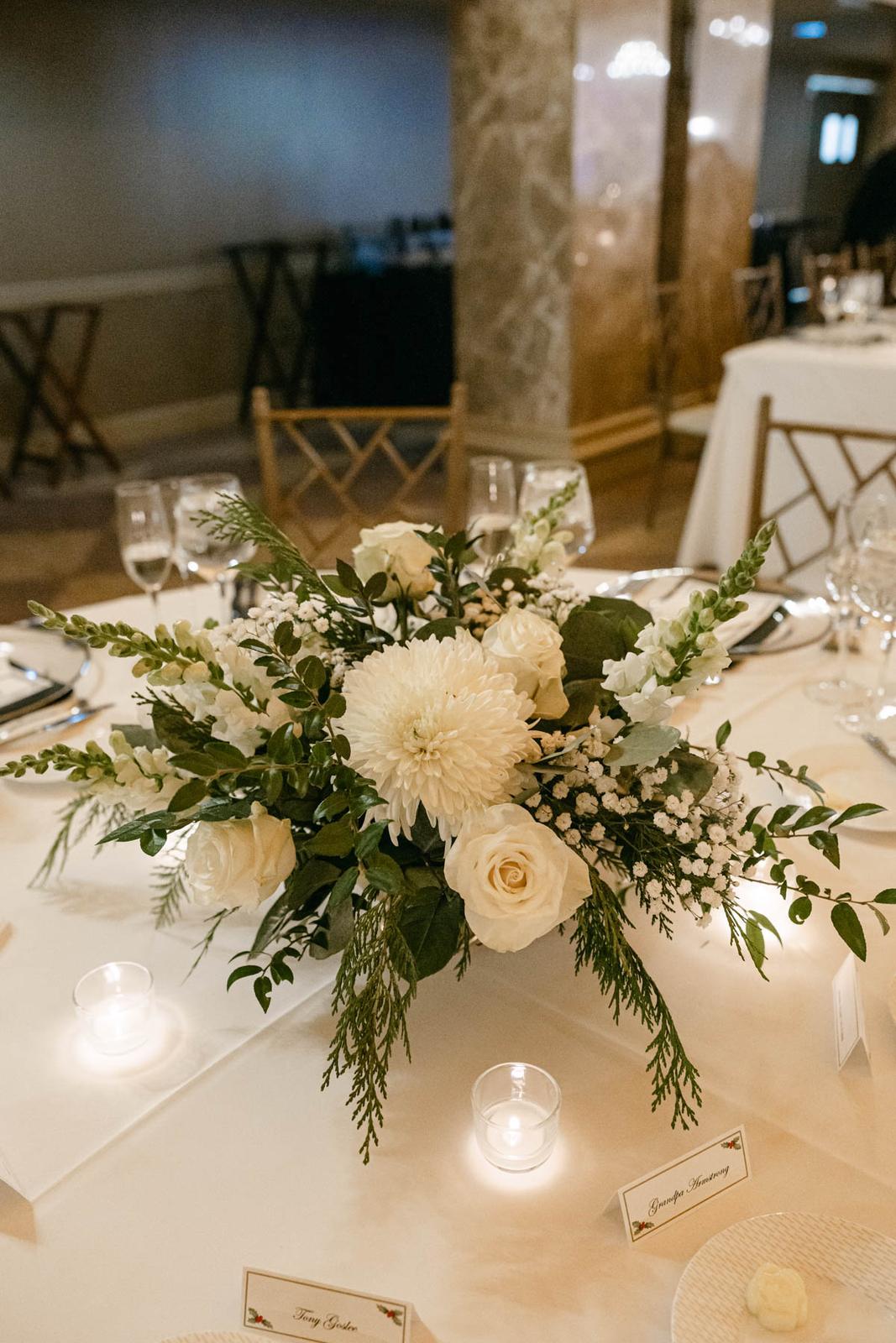 Low white wedding centerpiece with roses, disbuds, baby’s breath and greenery at The Coronado