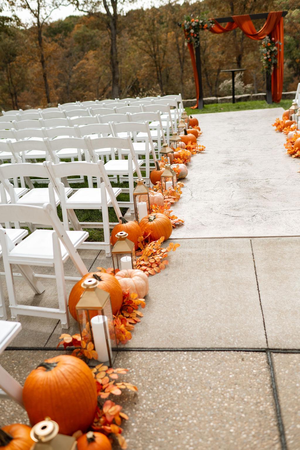 Wedding aisle lined with pumpkins, lanterns and autumn leaves