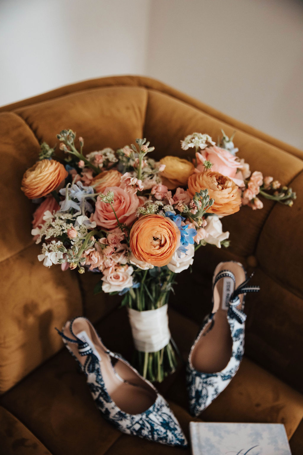 Bride holding a colorful wedding bouquet with peach ranunculus and soft blue flowers