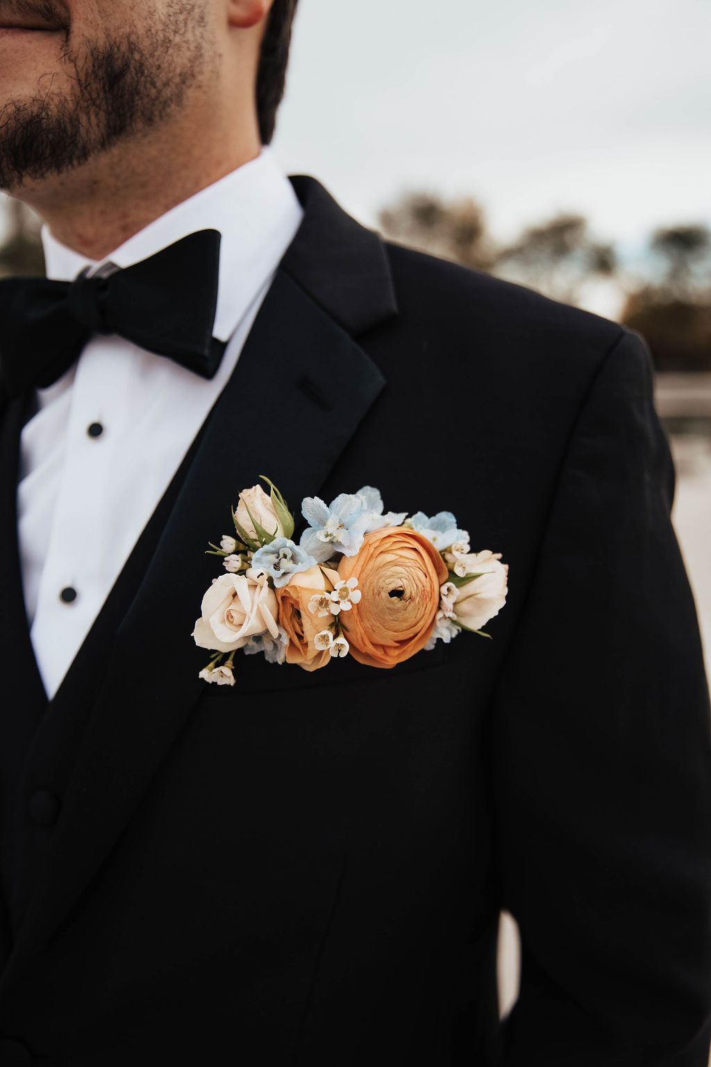 Groom wearing a peach ranunculus pocket boutonniere with blue and white accent flowers
