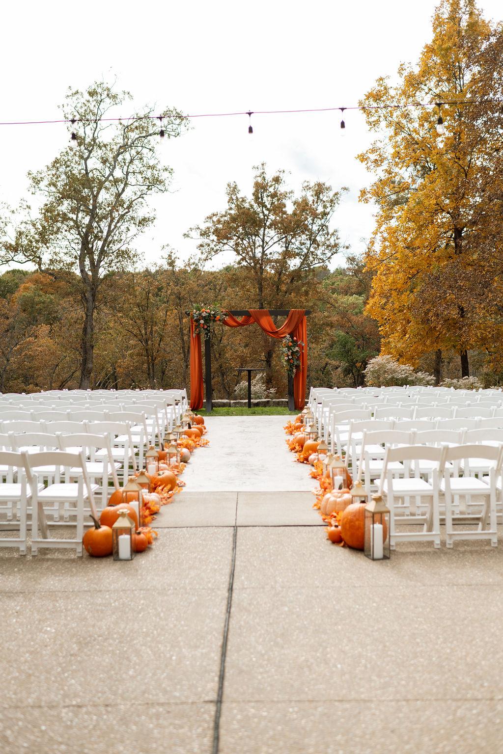 Outdoor autumn wedding ceremony with a pumpkin-lined aisle and floral arbor